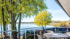 Une terrasse avec une table et des chaises, donnant sur une étendue d’eau et des arbres.
