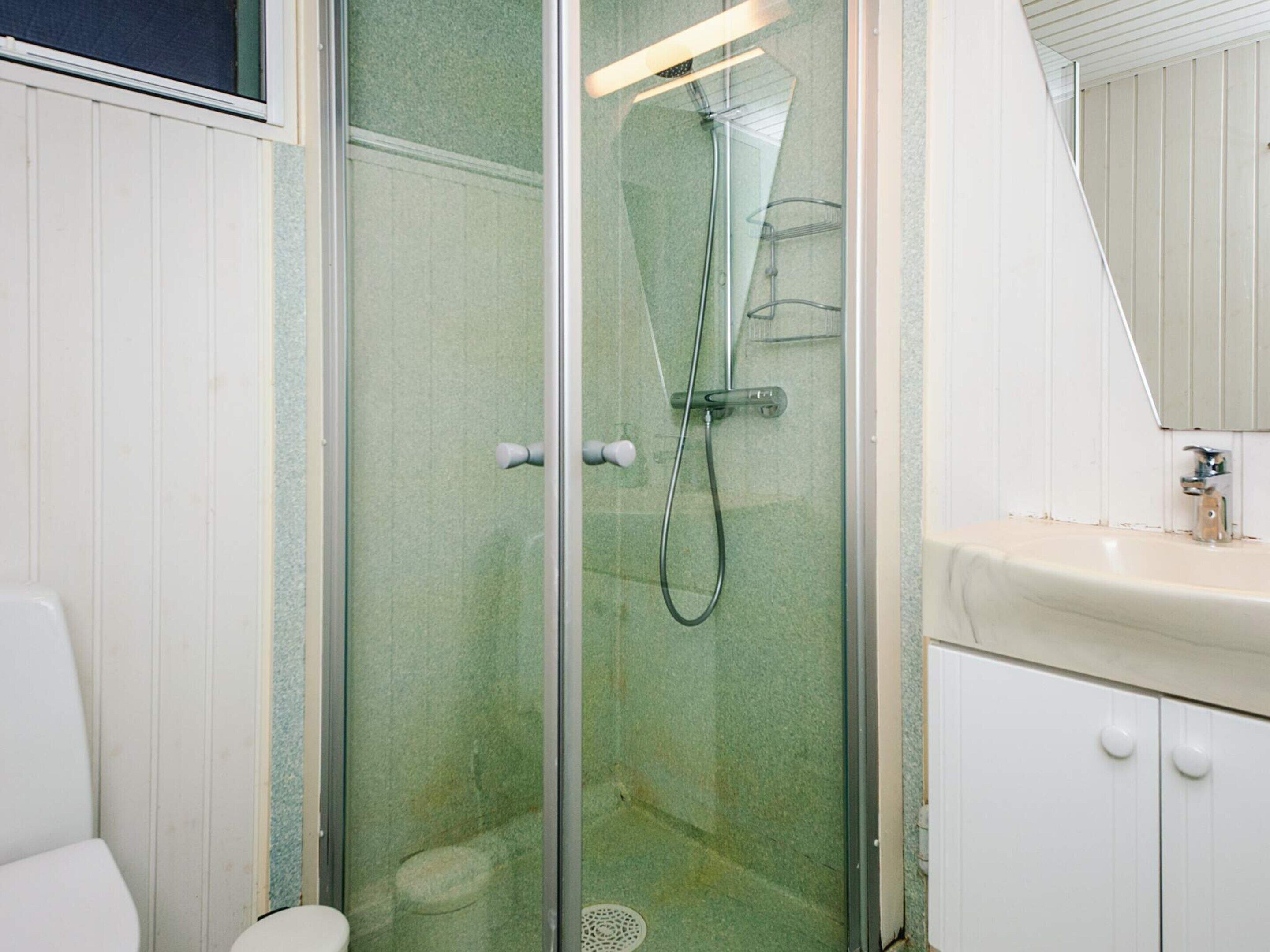 Ein Badezimmer mit Duschkabine, Toilette und Waschbecken mit Spiegel darüber.