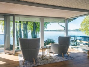 Une pièce moderne avec de grandes fenêtres, deux fauteuils gris, une petite table ronde et un tapis à motifs.