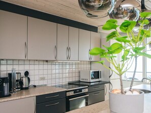Une cuisine moderne avec des meubles blancs, un four à micro-ondes, une cuisinière et une plante en pot.