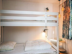 Une chambre avec un lit superposé, un radiateur, une lampe et une petite table sur laquelle se trouvent des bouteilles vertes.