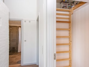 Un corridoio con una scala in legno che conduce a una zona mansardata, una porta bianca e un angolo doccia.