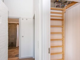 Un pasillo con una escalera de madera que lleva a un altillo, una puerta blanca y una zona de ducha.
