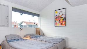 Quarto com cama, janela, cadeira e parede com um quadro colorido.