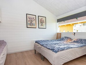 A bedroom with a bed, a chair, and two framed artworks on the wall.