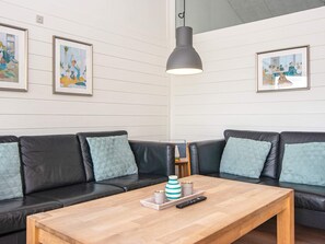 A modern living room with a wooden coffee table, black leather sofas, and framed artwork on the walls.