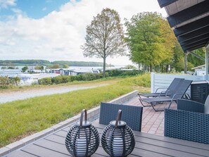 A deck with outdoor seating and two spherical lanterns, overlooking a body of water with boats and trees.