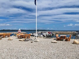 A pebbled beach with wooden benches and a flagpole.