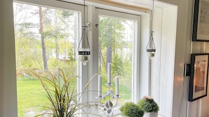 A room with a large window, white walls, and a white ceiling. There are three hanging lanterns, a potted plant, and two small potted plants on the windowsill. - 7 Person Holiday Home in Klassbol (Klässbol)