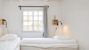 A room with two single beds, a window with a curtain, a wall-mounted lamp, and a small wooden shelf. - 10 Person Holiday Home in Marstal (Marstal)