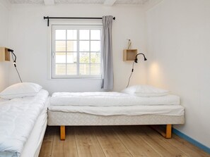 A room with two single beds, a window with a curtain, a wall-mounted lamp, and a small wooden shelf. - 10 Person Holiday Home in Marstal (Marstal)