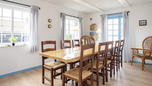A dining area with a wooden table and chairs, large windows with curtains, and a clock on the wall. - 10 Person Holiday Home in Marstal (Marstal)