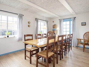 A dining area with a wooden table and chairs, large windows with curtains, and a clock on the wall. - 10 Person Holiday Home in Marstal (Marstal)