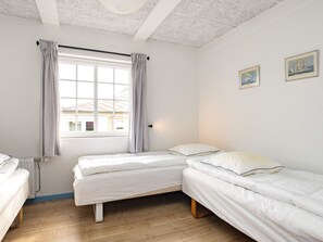 Ett rum med två separata sängar, ett fönster med gardiner, ett element och två inramade tavlor på väggen.