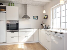 Una cocina moderna con armarios blancos, horno empotrado, campana extractora de acero inoxidable y ventana que proporciona luz natural.