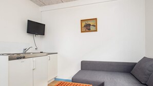 A compact living space with a kitchenette, a grey sofa, and a small wooden table. - 10 Person Holiday Home in Marstal (Marstal)