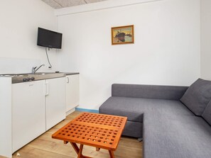 A compact living space with a kitchenette, a grey sofa, and a small wooden table. - 10 Person Holiday Home in Marstal (Marstal)