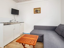 Un espacio habitable compacto con kitchenette, un sofá gris y una pequeña mesa de madera.