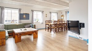 A spacious living room with a wooden coffee table, a sofa, a dining table with chairs, and a flat-screen TV mounted on the wall. - 10 Person Holiday Home in Marstal (Marstal)