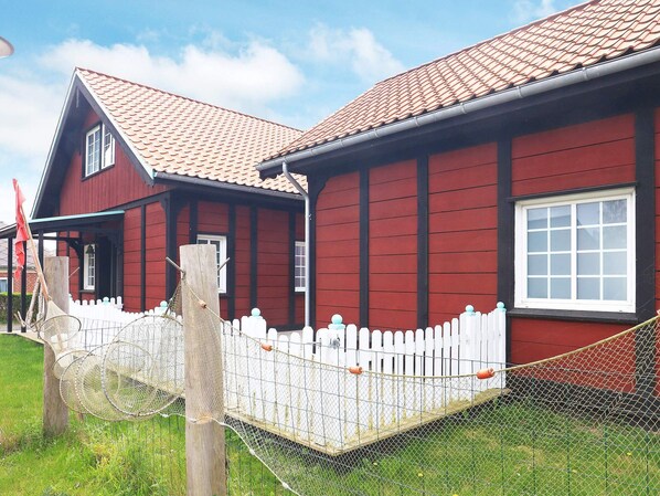 A red wooden house with a white picket fence and a metal gate. - 10 Person Holiday Home in Marstal (Marstal)