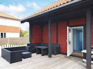 An outdoor patio with a red wall, a wooden deck, and a black outdoor furniture set.