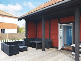 Un patio exterior con pared roja, cubierta de madera y juego de mobiliario exterior negro.