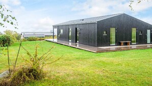 Un edificio moderno de color oscuro con techo plano, ventanas amplias y un espacio exterior cubierto con un banco.