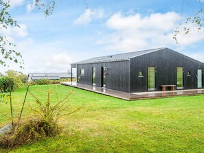 A modern, dark-colored building with a flat roof, large windows, and a covered outdoor area with a bench. - 6 Person Holiday Home in Ronde (Ronde)