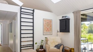 Un intérieur moderne avec un escalier, une œuvre d’art encadrée, un fauteuil confortable et une fenêtre donnant sur un paysage verdoyant.