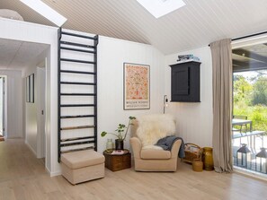 A modern interior with a staircase, a framed artwork, a cushioned chair, and a window with a view of greenery.