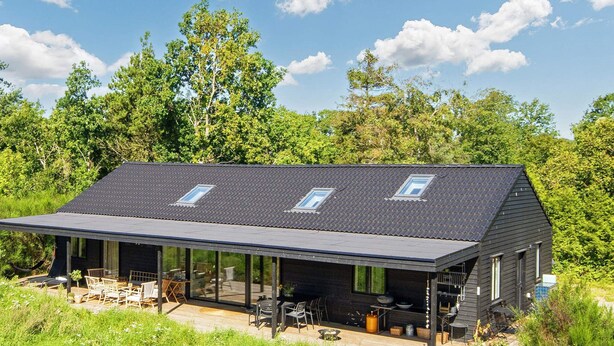 Une maison moderne dotée d’un toit en pente, de grandes fenêtres et d’un espace extérieur aménagé pour se détendre.