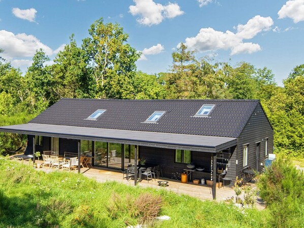 A modern house with a sloped roof, large windows, and an outdoor seating area.