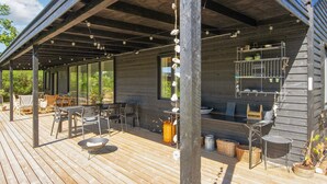 Une terrasse extérieure couverte, équipée d’un barbecue, d’un espace salon et de plantes en pot.