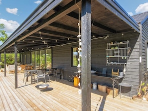 A covered outdoor deck with a grill, seating area, and potted plants.