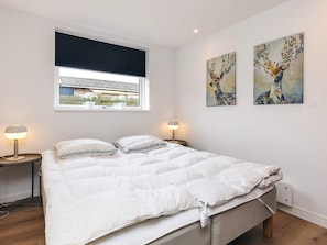 A bedroom with a large bed, two bedside tables with lamps, a window with a view of a building, and two wall-mounted paintings. - 4 Star Holiday Home in Vaeggerlose (Vaeggerlose)