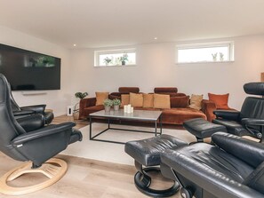 A modern living room with a brown sofa set, black leather chairs, a coffee table, and a flat-screen TV mounted on the wall. - 4 Star Holiday Home in Vaeggerlose (Vaeggerlose)