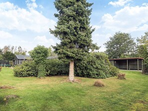 A large coniferous tree in a well-maintained grassy area with a small shed and a fence in the background. - 4 Star Holiday Home in Vaeggerlose (Vaeggerlose)