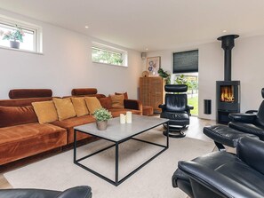 A modern living room with a brown sofa, a black leather chair, a coffee table, and a black wood-burning stove. - 4 Star Holiday Home in Vaeggerlose (Vaeggerlose)