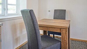 A dining area with a wooden table and two chairs, a window with white frames, a wall clock, and a light fixture. - 14 Person Holiday Home in Ronne (Akirkeby)