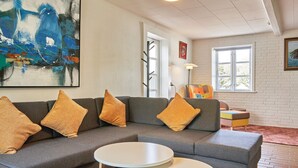 A modern living room with a sectional sofa, two round tables, and a large abstract painting. - 14 Person Holiday Home in Ronne (Akirkeby)