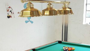 A pool table with a single white ball and colorful balls, a brass overhead lamp, and a wall with a Superman drawing. - 14 Person Holiday Home in Ronne (Akirkeby)