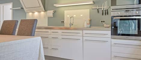 A modern kitchen with white cabinetry, a built-in oven, and a dining area with a table and chairs.
