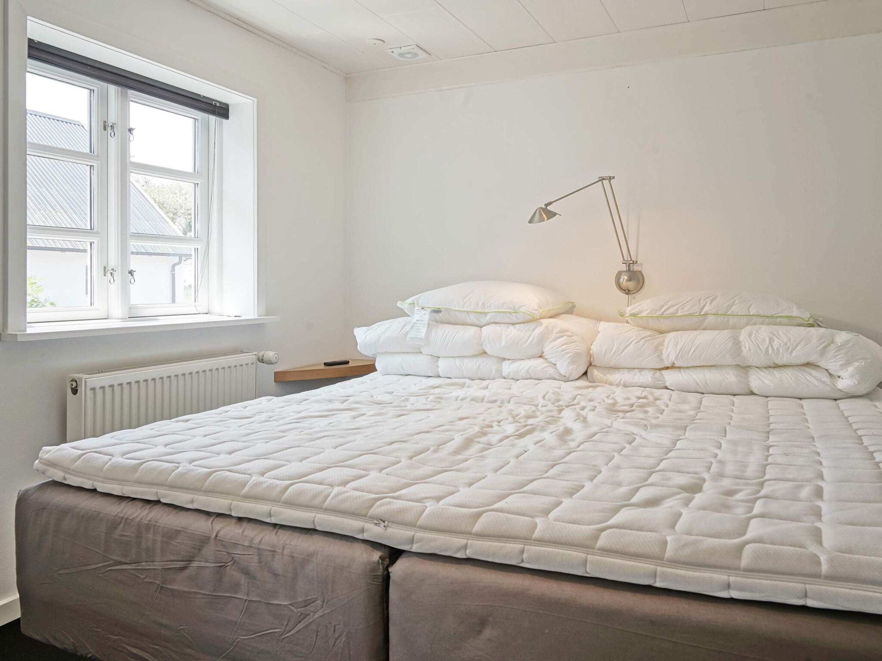 Un dormitorio con cama, mesita de noche, lámpara y ventana.