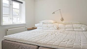 Un dormitorio con cama, mesita de noche, lámpara y ventana.