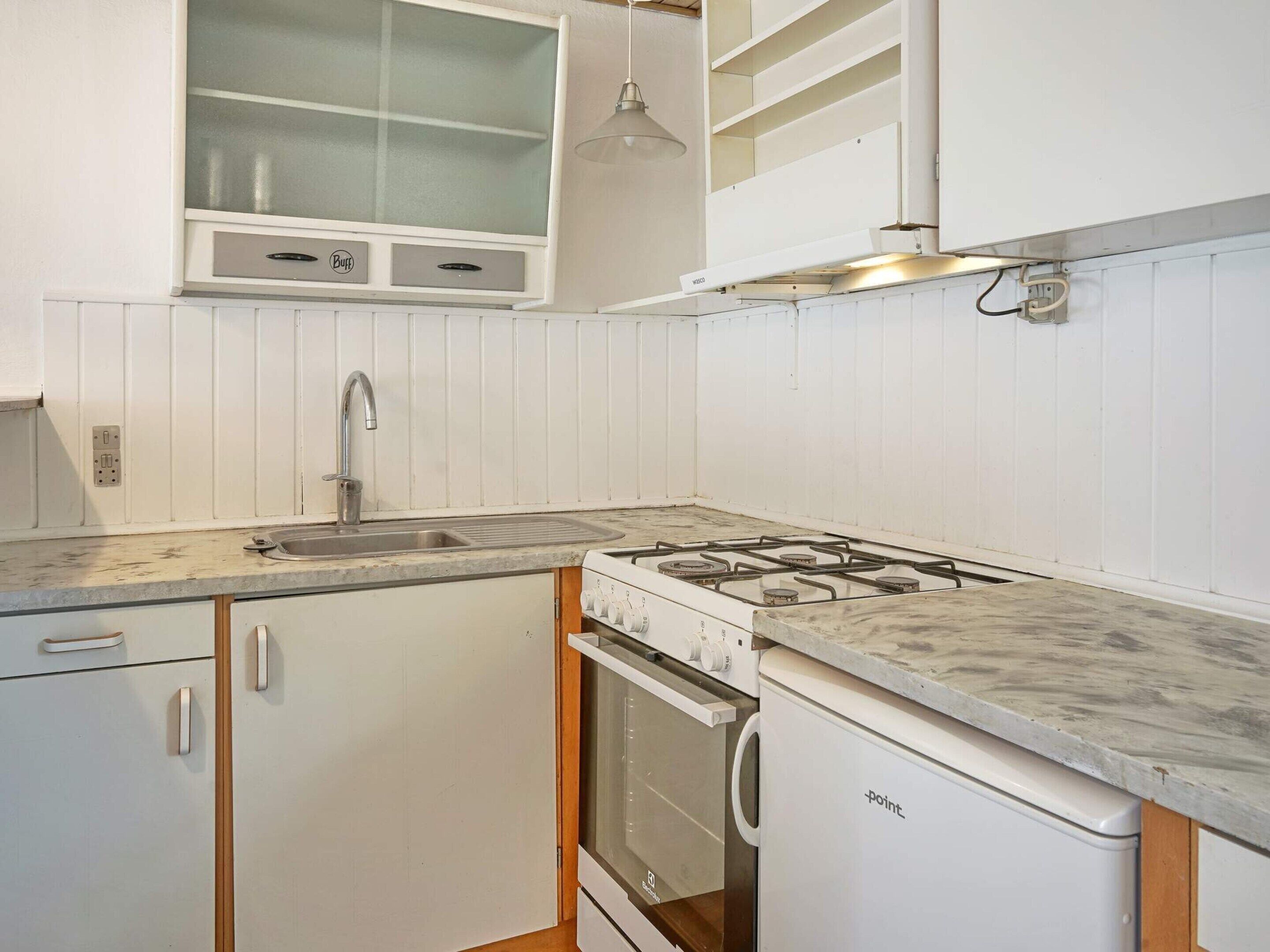 A kitchen with a gas stove, oven, sink, and white cabinetry.