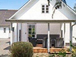 Un espacio de estar al aire libre cubierto con mobiliario de mimbre, una terraza de madera y un edificio blanco con una ventana.