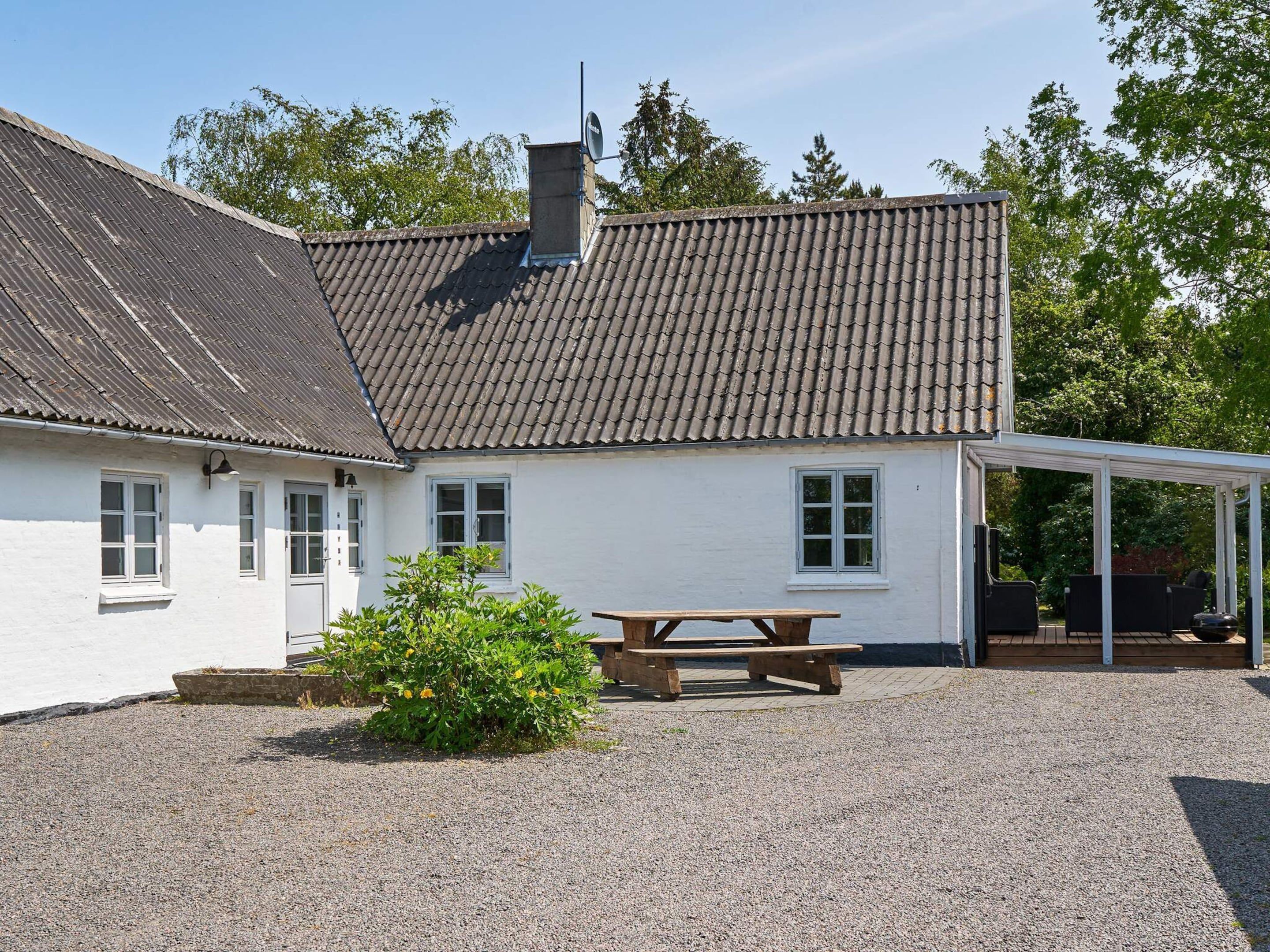 A white building with a tiled roof, a covered outdoor seating area, and a gravel driveway.