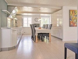 Una cocina moderna con armarios blancos, una zona de comedor con mesa y sillas, y un gran ventanal que proporciona luz natural.