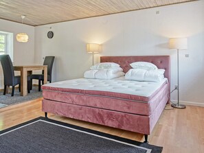 Quarto com cama de casal, luminárias de cabeceira, teto de madeira, mesa de jantar com cadeiras e tapete.
