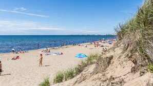 A beach with people sunbathing and swimming, a clear sky, and a grassy dune. - 7 Person Holiday Home in Falkenberg (Falkenberg)